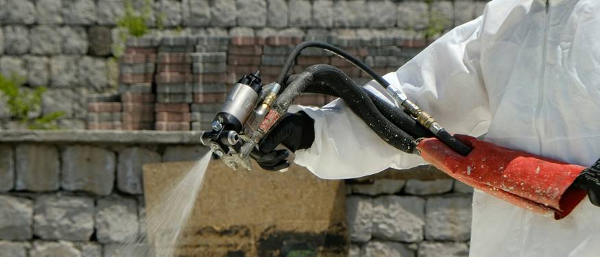 A technician or homeowner using protective gear to remediate mold on a wall, with tools and plastic sheeting visible